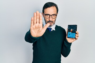 Poster - Middle age hispanic man holding hdd disk with open hand doing stop sign with serious and confident expression, defense gesture