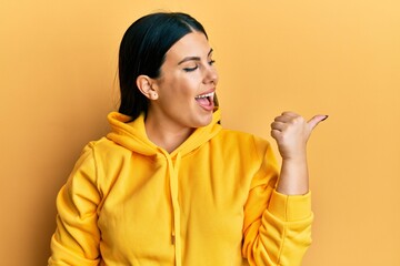 Poster - Beautiful brunette woman wearing casual sweatshirt pointing thumb up to the side smiling happy with open mouth