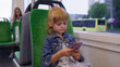© Andrii Iemelianenko - Joyful child girl citizen playing on smartphone, chatting, texting, browsing social media while traveling by bus to city center. Public transport. Urban lifestyle. Young kid passenger at modern tram