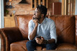 © fizkes - Thoughtful millennial African guy with mobile phone looking at window, sitting on leather couch at home, holding smartphone, thinking over text message for online chat, smiling at thoughts