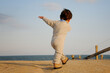 Outdoor Fall portrait of back of toddler boy swinging arms joyfully while walking up hill in sand towards beach