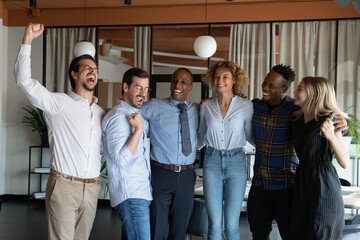 Wall Mural - Excited diverse multiethnic businesspeople feel euphoric celebrate mutual team win or victory in office. Smiling overjoyed multiracial employees triumph with good business results or shared success.