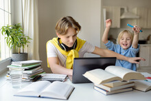 Teenager Boy Study At Home And His Younger Brother Screams And Interrupts Him. Online Education And Distance Learning For High School Students. School Boy Doing His Homework