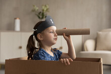 Funny Cute Kid Girl Playing Pirate At Home. Little Child In Buccaneer Black Hat Sailing In Cardboard Box Boat, Looking Forward Through Toy Spyglass. Childhood, Role Game, Costume Party
