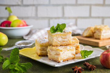 Sliced apple pie made from shortcrust pastry with cottage cheese cream and apple wedges on a square plate on a green concrete background. Apple pie recipes.