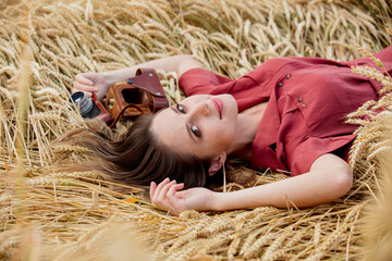 Sticker - young woman in red dress with camera is lying on spikelets of wheat field