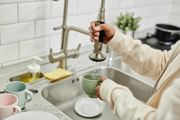 Close up of young African-American woman washing dishes at home while doing chores on weekend, copy space