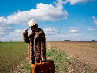 Sticker - Woman in coat with suitcase on field with wind turbines