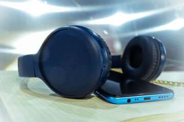 Blue smart headphones and a smart phone lie on an open notebook against the background of bright glare of spotlights 