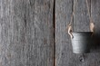 An empty metal pail hanging from twine against a rustic wood wall.