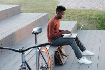 Aufkleber - Young serious businessman looking at laptop screen while typing in urban environment