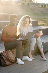 Poster - Two young successful colleagues preparing presentation while sitting on staircase on sunny day