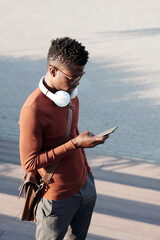 Poster - Young African businessman in smart casualwear scrolling in smartphone after work on summer day