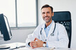 © baranq - Portrait of cheerful doctor sitting in office and looking at camera