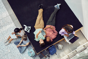 Wall Mural - Top down view at diverse group of kids relaxing and using gadgets during break at modern school