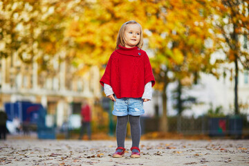 Wall Mural - Adorable little girl in red poncho walking in autumn park on a sunny fall day.