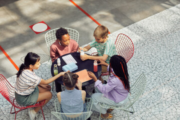 Wall Mural - High angle view at diverse group of kids sitting at table outdoors during lunch at modern school, copy space