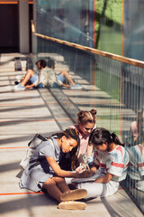 Wall Mural - Vertical portrait of schoolkids doing homework while sitting on floor in school lit by sunlight, copy space