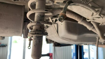 Poster - The car is in a car service station for the repair of the brake system. Brake fluid drips from the hose. The car is suspended on a lift in a car service station.