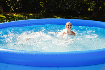 A child is having fun in a rubber pool. A girl splashes in the pool in the garden.