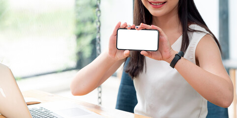 Wall Mural - cropped shot of woman hand holding smartphone and showing blank screen while sitting at the table at