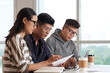 © DragonImages - Group of college students drinking coffee and reading project documents at desk in class