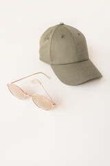 Wall Mural - Beige cap and sunglasses on white background. Female fashion cloth and accessory concept. Neutral dusty colour