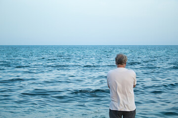 view from behind of mature man with grey hair enjoying on seashore and looking at the horizon