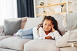 © standret - Laying down on the sofa. Little girl in casual clothes is at home alone