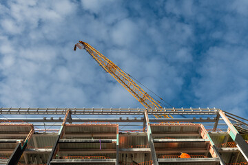 apartment under construction with orange crane, low angle view. blue sky with fluffy white clouds.