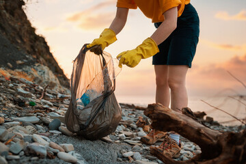 Wall Mural - Earth Day. Close up of volunteer's hands in rubber gloves puts a dirty plastic bottle in bag. Sunset on the background. The concept of ecology disaster