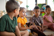 © Halfpoint - Group of small nursery school children sitting on floor indoors in classroom, listening to teacher.
