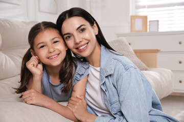 Canvas Print - Young mother and her daughter on sofa in living room. Adoption concept