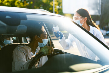 Wall Mural - Health worker wearing face mask measuring temperature to black woman