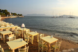 Fototapeta Do akwarium - tables set for dinner on the beach at sunset over the sea in Aegina in Greece