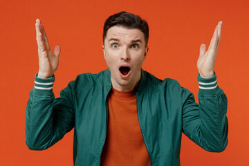 Wall Mural - Angry shocked unnerved aggrieved disconcerted young brunet man 20s wear red t-shirt green jacket spreading hands isolated on plain orange background studio portrait. People emotions lifestyle concept