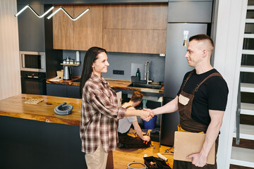 Wall Mural - Happy young woman shaking hand of plumber after repairing work