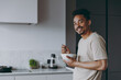 © ViDi Studio - Young happy smiling bachelor african american man in casual clothes eat breakfast muesli cereals with milk fruit in bowl prepare cook food in light kitchen at home alone indoor. Healthy diet concept