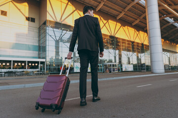 Wall Mural - Full length back view young traveler businessman man 20s wear black classic suit walking going outside at international airport terminal with suitcase valise Air flight business trip lifestyle concept