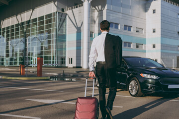 Wall Mural - Bottom back view young traveler businessman young man wearing black dinner suit walk go outside at international airport terminal with suitcase to car booking taxi Air flight business trip concept