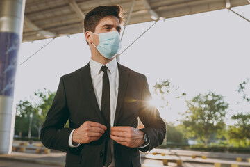 Wall Mural - Bottom view sunlit serious young traveler businessman man 20s wear black dinner suit sterile mask stand outside at international airport terminal look aside. People air flight business trip concept