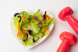 Closeup of a small plate of salad with pink dumbbells on white background.