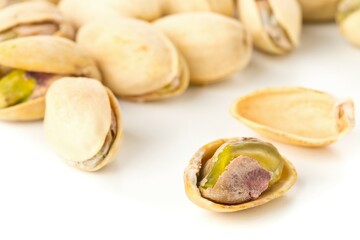 Wall Mural - Close up of single, open pistachio in front of heap of salted, roasted green pistachio nuts snack over white background, healthy food snack