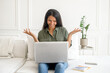 © Vadim Pastuh - Smiling optimistic young indian female freelancer or a student sitting on the couch with laptop on the lap, happy young eastern woman taking a part in virtual meeting, video calling and talking online