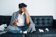 © baranq - Sick man blowing running nose sitting on sofa at home