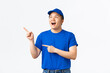 Excited and amazed asian delivery guy in blue t-shirt and cap, company uniform, pointing and looking upper left corner with euphoric, thrilled expression, see awesome promo, white background