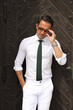 Bardzo przystojny, elegancki mężczyzna w białej koszuli i zielonym krawacie i okularach przeciwsłonecznych.