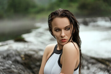 Wall Mural - Sexy Caucasian brunette woman with wet hair posing in a white swimsuit on the beach