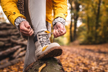 Woman tying shoelace on her hiking boot. Tourist is getting ready for autumn hike at woodland trekking trail