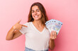 © Asier - Young caucasian woman holding bills isolated on pink background  person pointing by hand to a shirt copy space, proud and confident